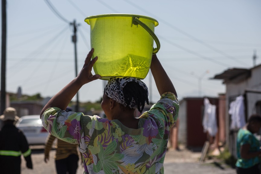 A resident walking with water from a tap back to her home. Despite promised upgrading for more than fifteen years, residents on this site still rely upon only a few shared taps. Photo by Shachaf Polakow.